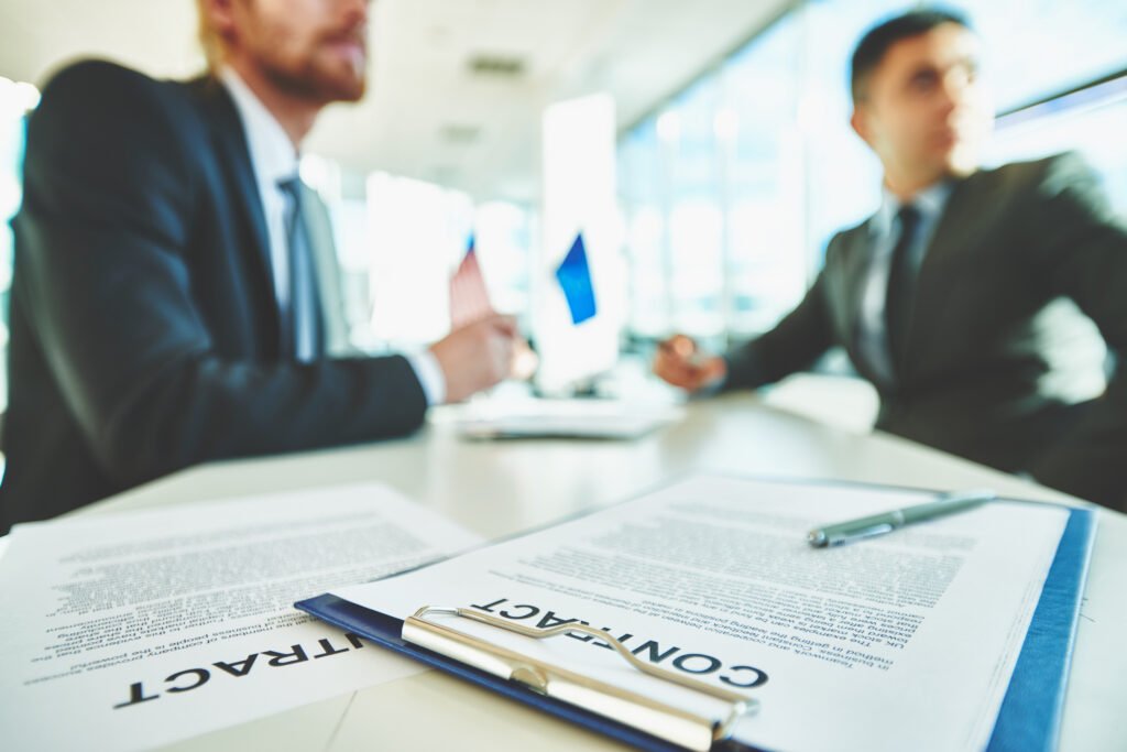 Two businessmen reviewing contracts at a desk with a pen and documents in front of them.